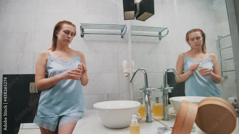 Young beautiful elegant woman in delicate lovely lingerie standing by window sink, applying moisturizing toner lotion on face, using cotton disc for massaging. Face routine. Young beautiful elegant woman in delicate lovely lingerie standing by window sink, applying moisturizing toner lotion on face, using cotton disc for massaging. Face routine.
