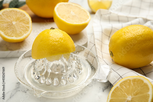 Glass squeezer and fresh lemons on white marble table