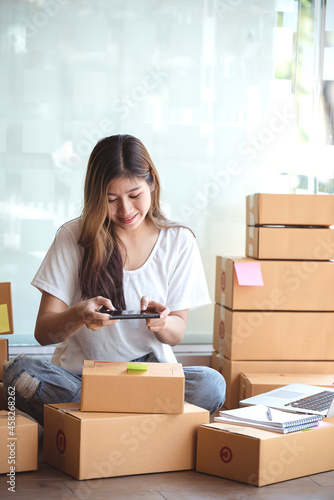 Young woman taking pictures during packaging with a mobile phone or smartphone digital camera to prepare the product box pack selling ideas online