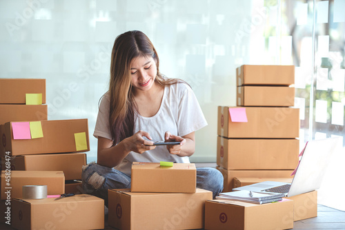 Young woman taking pictures during packaging with a mobile phone or smartphone digital camera to prepare the product box pack selling ideas online © Daenin