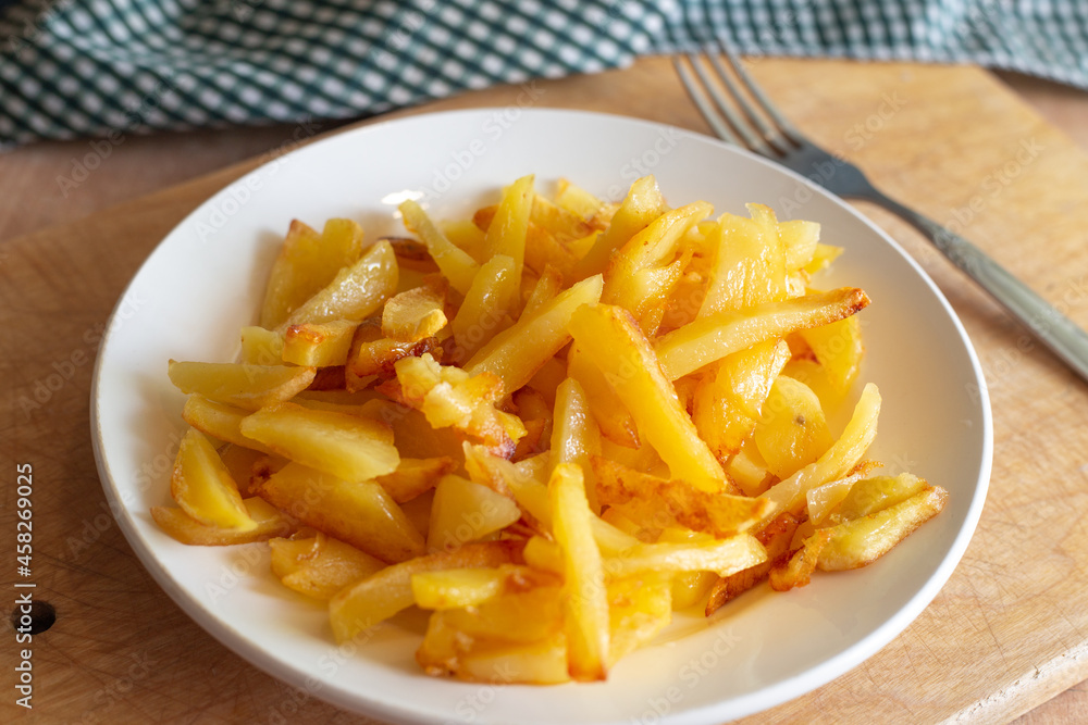 Fresh golden fried potatoes in a white plate on a wooden stand. Delicious vegetable dish Fresh golden fried potatoes in a white plate on a wooden stand. Delicious vegetable dish