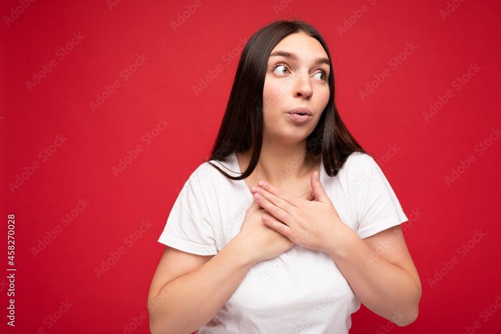 Obraz premium Photo of shocked amazed sorrowful young beautiful brunette female person with sincere emotions wearing casual white t-shirt for mockup isolated over red background with copy space