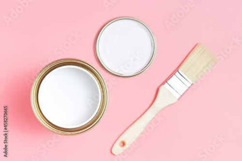 Open paint can and paintbrush on pink background top view.