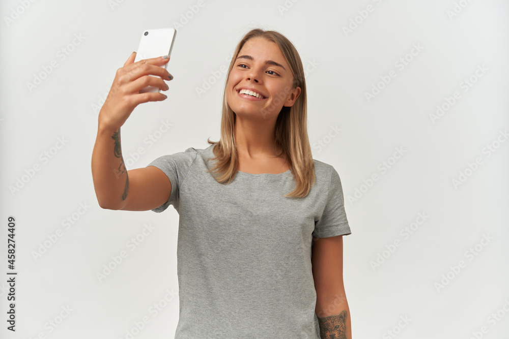 Portrait of young brunette female with perfect smile, wears gray t-shirt, making selfie. isolated over white background Portrait of young brunette female with perfect smile, wears gray t-shirt, making selfie. isolated over white background