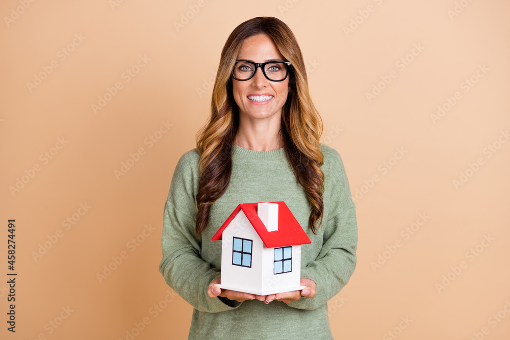 Photo portrait woman wearing glasses smiling keeping little house isolated pastel beige color background Photo portrait woman wearing glasses smiling keeping little house isolated pastel beige color background