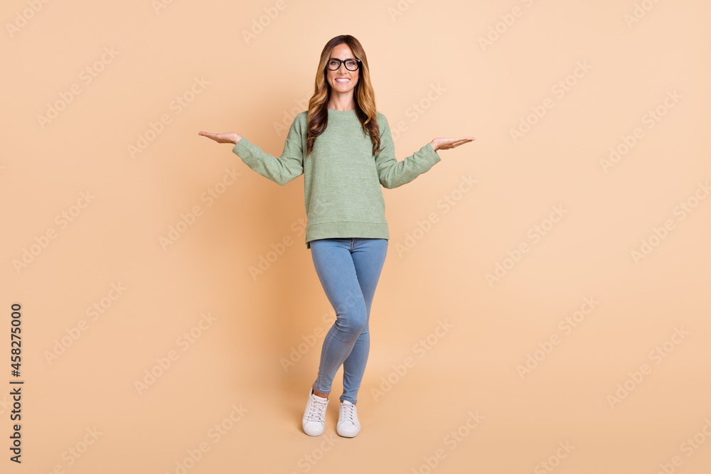 Full length body size view of attractive cheerful wavy-haired woman holding copy space isolated over beige pastel color background Full length body size view of attractive cheerful wavy-haired woman holding copy space isolated over beige pastel color background