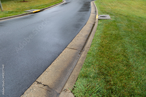 Long view of wet roadway on a rainy day, long street with wet asphalt edged with formed concrete curbs and storm drains, creative copy space, horizontal aspect
