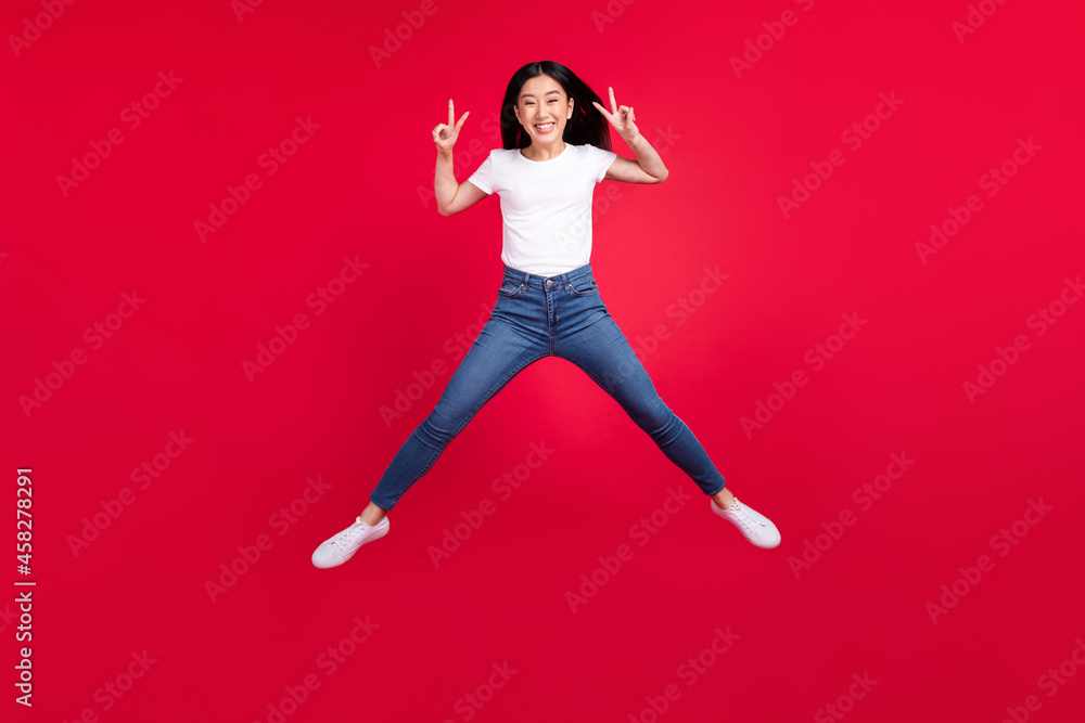 Full body photo of young excited asian girl happy positive smile show peace cool v-sign jump isolated over red color background Full body photo of young excited asian girl happy positive smile show peace cool v-sign jump isolated over red color background