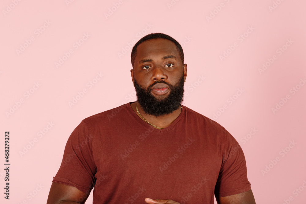 Handsome bearded African-American model man in brown t-shirt looks to camera on pink background in studio Handsome bearded African-American model man in brown t-shirt looks to camera on pink background in studio