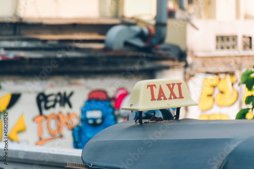 A taxi sign on a tuk-tuk's canvas roof and blur the background of the graphic wall