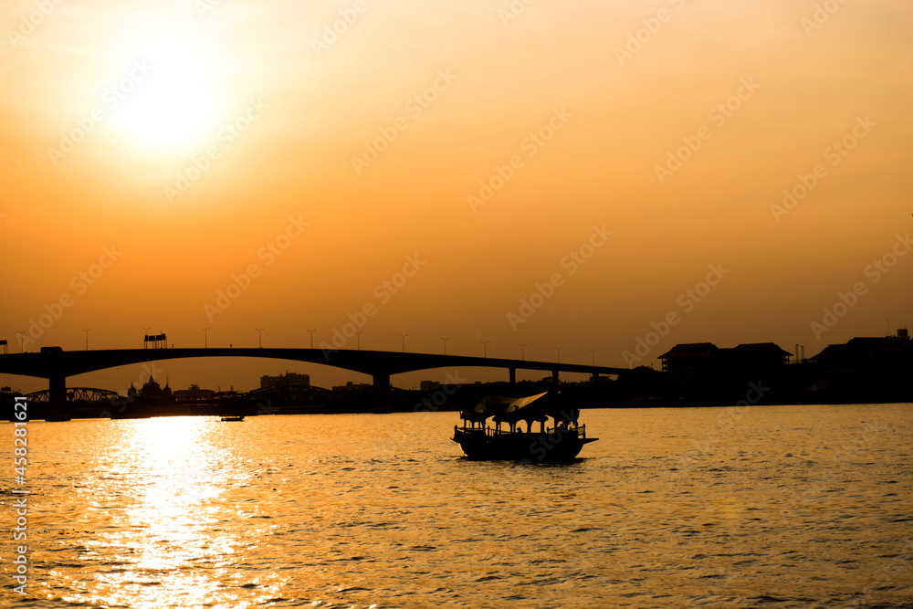 Silhouette of a boat floating in the water and a large bridge behind.
