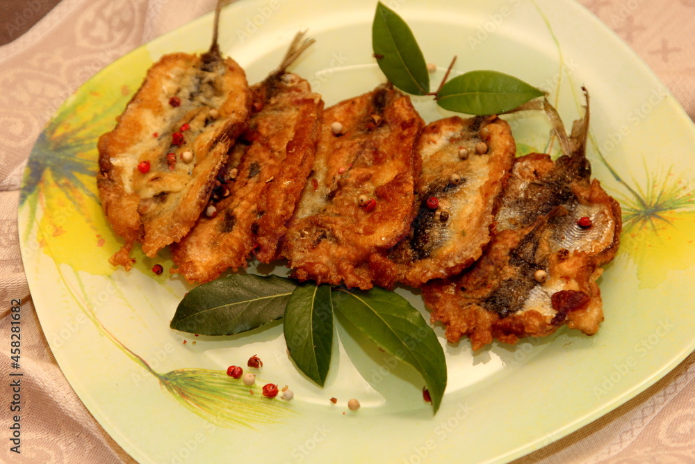 Crispy deep fried small fish on a plate, decorated with bay leaves and spices. Dough herring. Herring recipes
