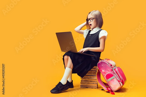 Full length shocked schoolgirl sit on the stack of books work on laptop. Kids education concept. photo
