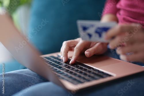 Woman typing on laptop keyboard and holding credit bank card in her hands closeup