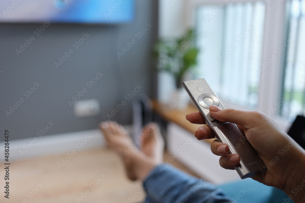 Woman is sitting on sofa and holding TV remote control in her hands closeup Woman is sitting on sofa and holding TV remote control in her hands closeup