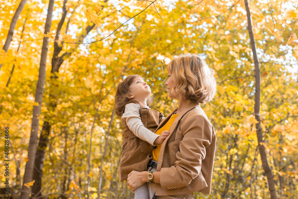 Fototapeta premium Young mother with her little daughter in an autumn park. Fall season, parenting and children concept.