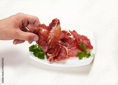 A man's hand takes a piece of jerky from a white plate.