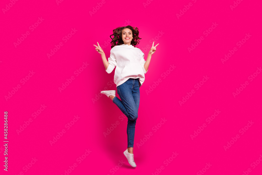 Photo of inspired active lady jump show v-sign wear white hoodie jeans footwear isolated pink color background