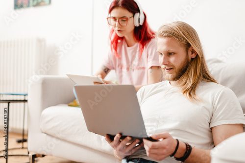 White man and woman using gadgets while sitting on couch and floor