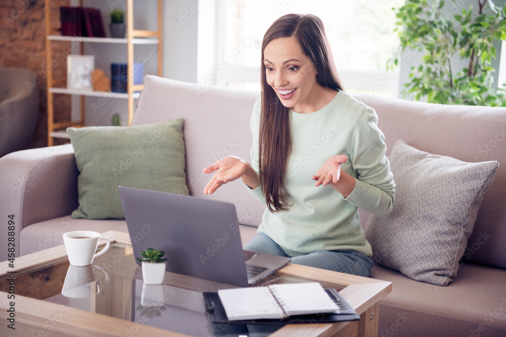 Photo of pretty funny young woman dressed turquoise sweater sitting sofa communicating modern device smiling indoors home room Photo of pretty funny young woman dressed turquoise sweater sitting sofa communicating modern device smiling indoors home room