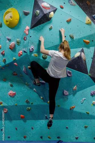 Young woman training on practice rock climbing wall indoor