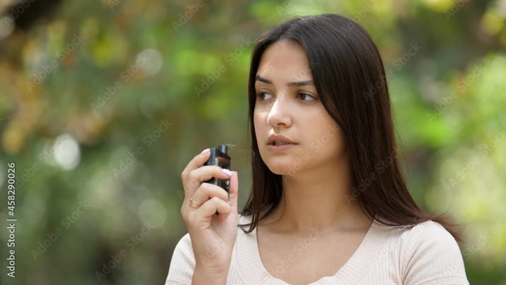 Gorgeous young woman standing and smoking e-cigarette in a green park Gorgeous young woman standing and smoking e-cigarette in a green park