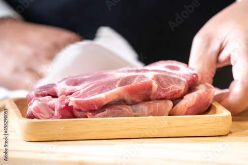 Raw Pork is prepared for Cook, It is on wood plate in studio light with Chef hand background.