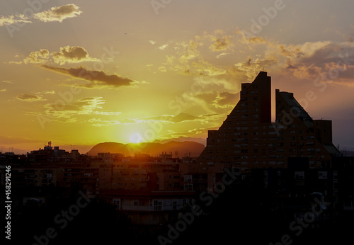 Atardecer con tonos amarillos, nubes y la silueta del edifico de la pirámide en Alicante