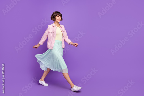 Full length photo of positive cheerful woman look go empty space weekend smile isolated on violet color background © deagreez