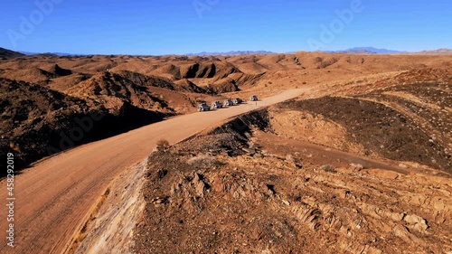 Srone shot of group of suv on desert serpentine road. Tourists having halt during expidition in african national park. Travellers exploring beauty of nature around cliffs and canyon shot by drone. photo