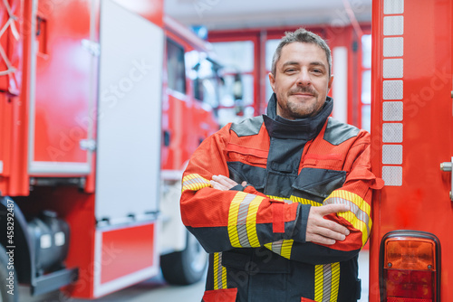 Canvas-taulu Experienced fire fighter man standing in front of fire truck with arms crossed