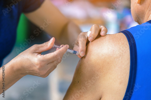 Close up to female doctor holding syringe making covid 19 vaccination injection dose in shoulder of senior man. Vaccinating elderly patient, healthcare concept. Covid-19 or coronavirus vaccine.