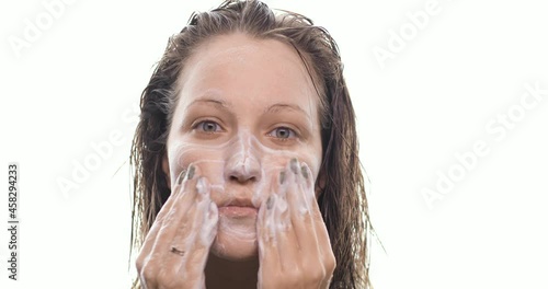 Portrait of young woman washing face with foamy gel. The girl with wet hair cleanses the skin after taking a shower, makes massage movements. Beauty treatments, spa, health and skin care concept.