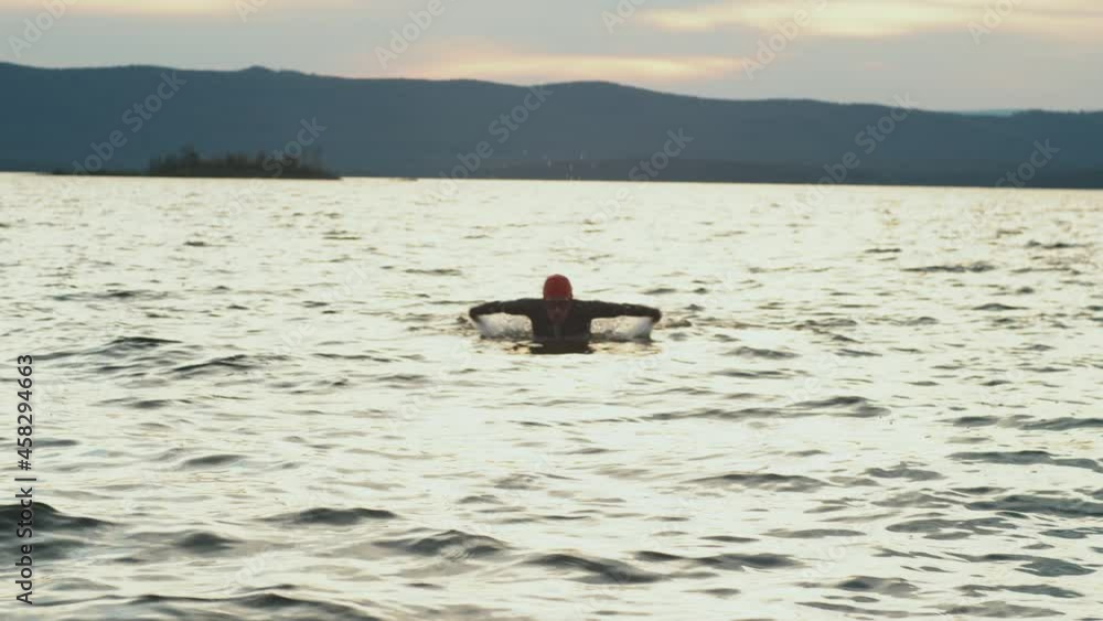 Female triathlete in wetsuit, cap and goggles swimming with butterfly stroke towards the camera in lake Female triathlete in wetsuit, cap and goggles swimming with butterfly stroke towards the camera in lake