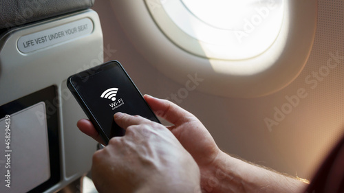 Close up Caucasian's hand holding smart phone sitting by the airplane window tap on the screen with wi-fi onboard signal. Internet wifi service during the flight, flight mode internet service concept