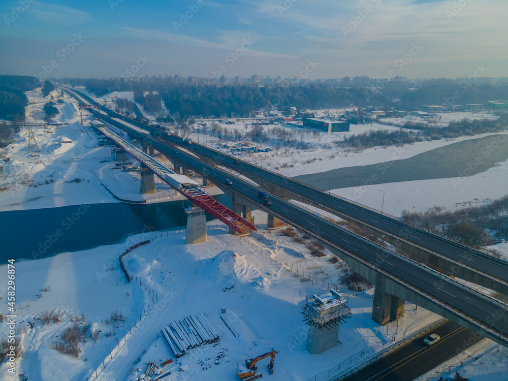 Obraz premium Aerial view of the bridge under construction over the river in winter with huge traffic. New bridge is being built next to the old one
