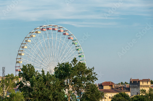 Ferris wheel or panoramic observation wheel in Avignon, France, and medieval city walls with towers on the background