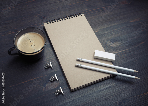 Blank stationery template. Photo of blank kraft notebook, pencils, eraser and coffee cup on wood table background.