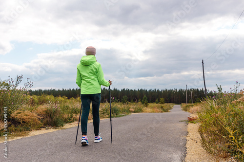 a woman in a light green windbreaker with Poles for Nordic walking stands with her back