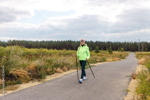 smiling five-year-old woman walks along the track with poles for Nordic walking