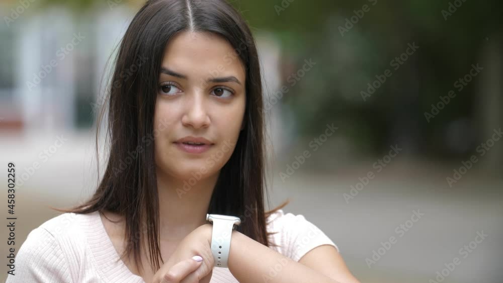 Smart girl speaking to her wristwatch and looking aside outdoors in summer Smart girl speaking to her wristwatch and looking aside outdoors in summer