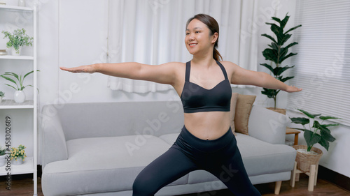 Portrait of gorgeous young asian woman practicing yoga at home stretching out while following a yoga routine