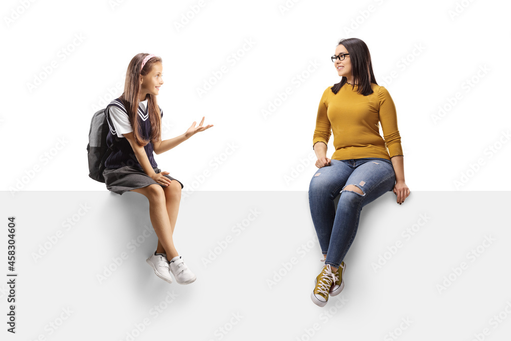 Schoolgirl and a young female sitting on a blank panel and having a conversation Schoolgirl and a young female sitting on a blank panel and having a conversation