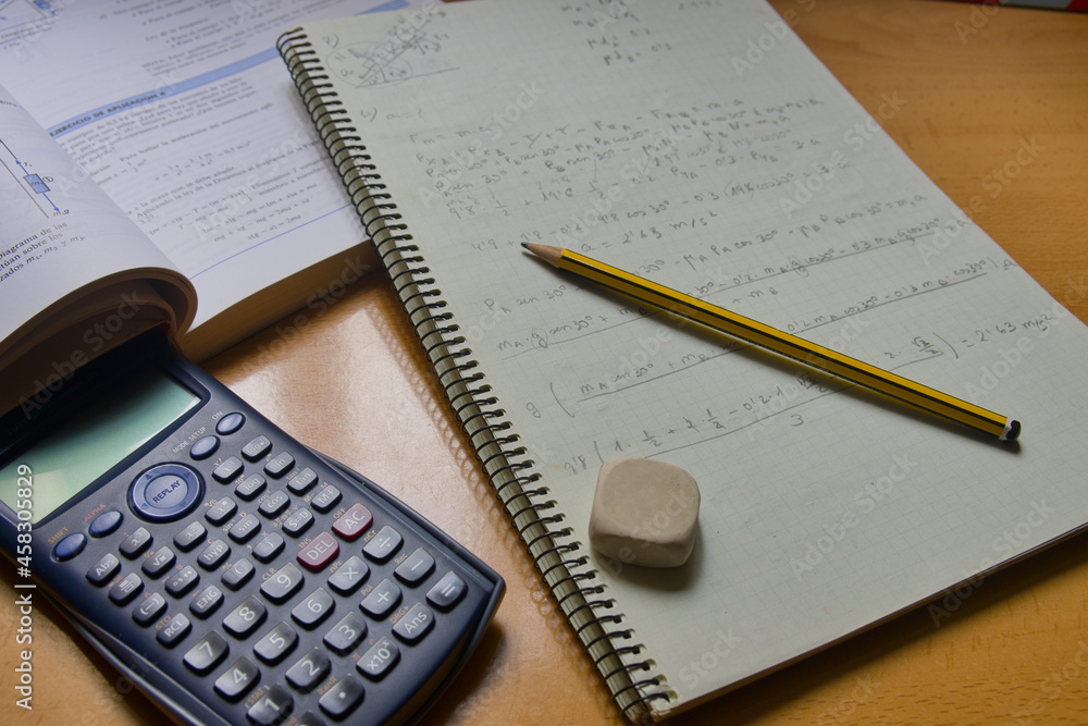 Student notebook with exercises next to a calculator, pencil, eraser and the textbook Student notebook with exercises next to a calculator, pencil, eraser and the textbook