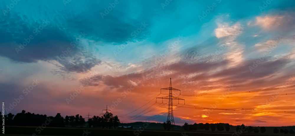 Beautiful sunset with a dramatic sky and overland high voltage lines near Eichendorf, Bavaria, Germany