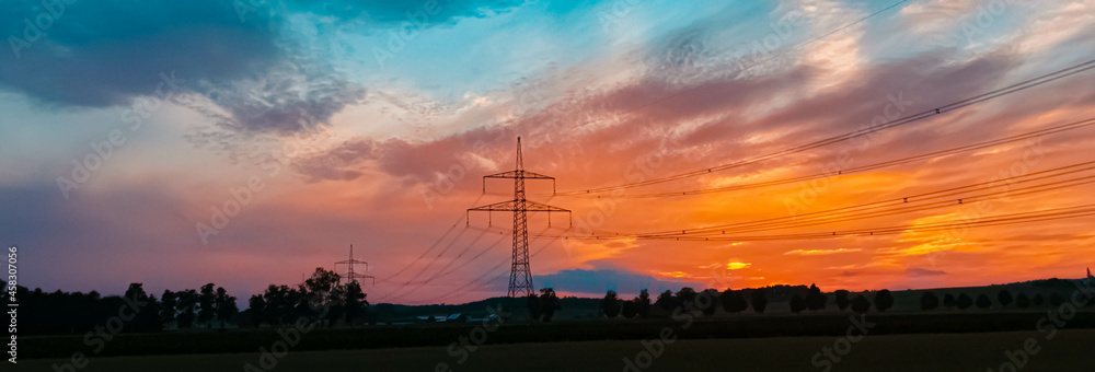 Beautiful sunset with a dramatic sky and overland high voltage lines near Eichendorf, Bavaria, Germany