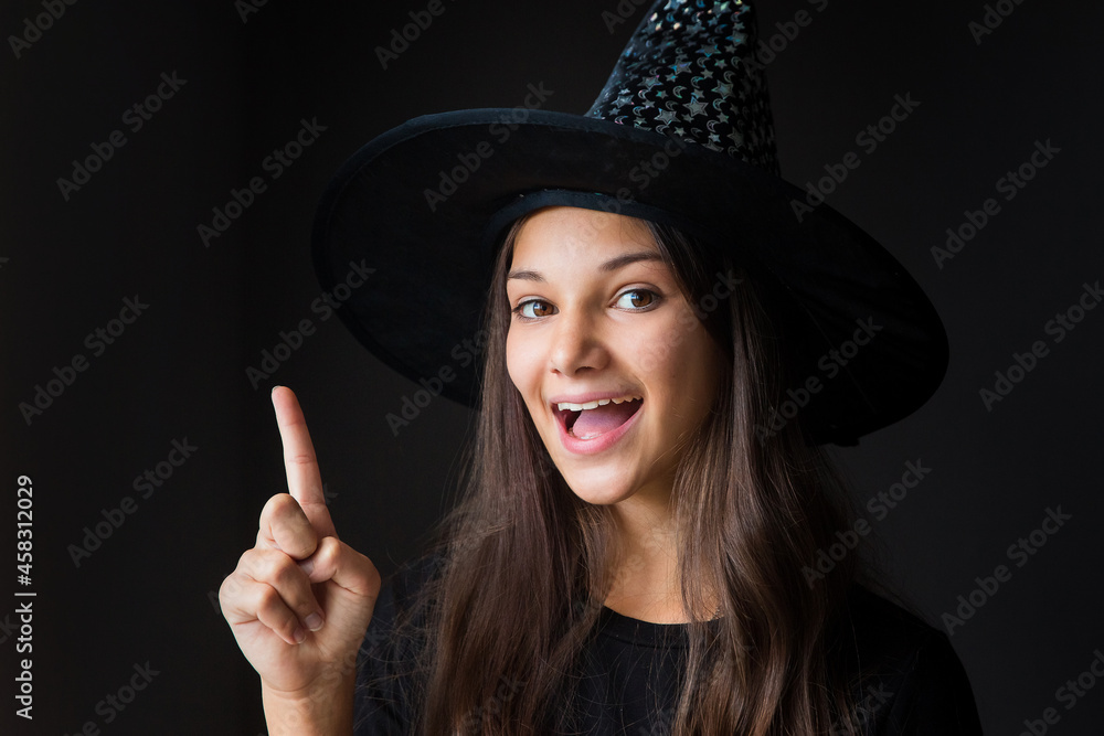 portrait of a smiling girl with her hand pointing up in a witch costume for Halloween close-up on a dark background
portrait of a smiling girl with her hand pointing up in a witch costume for Halloween close-up on a dark background
