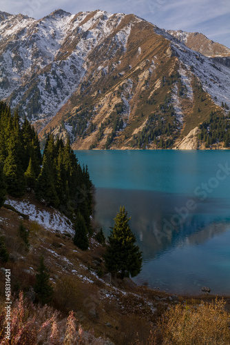 Mountain lake with blue water and tall fir trees on the shore in an autumn morning