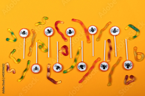 Halloween candy with black spiders,cobweb and tasty jelly worms on orange color background,top view