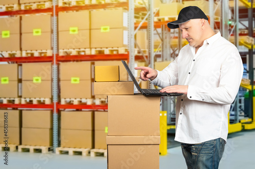 Warehouse manager during work. Logistic warehouse employee. Warehouse manager with laptop. Businessman with laptop near boxes. Logistics center worker on background boxs. Distribution Center Manager